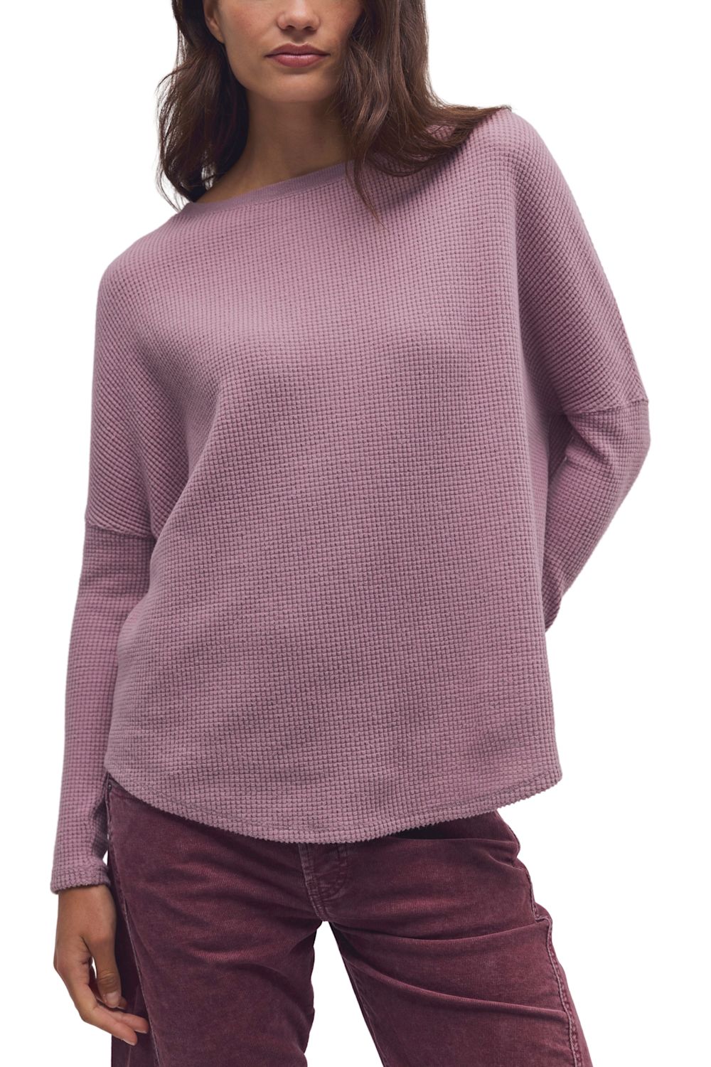 A woman wearing a textured, waffle-knit long-sleeve sweater in a dusty mauve-pink color, paired with dark burgundy pants, against a plain white background.