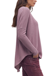 A woman shown from the side wearing a dusty mauve waffle-knit long-sleeve top and dark mauve corduroy pants against a plain white background.