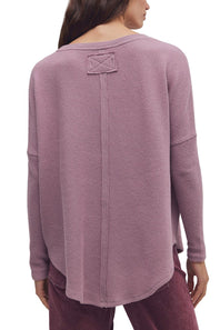 A woman shown from the back wearing a dusty mauve waffle-knit long-sleeve top with a small decorative patch detail on the upper back, paired with dark mauve pants against a plain white background.