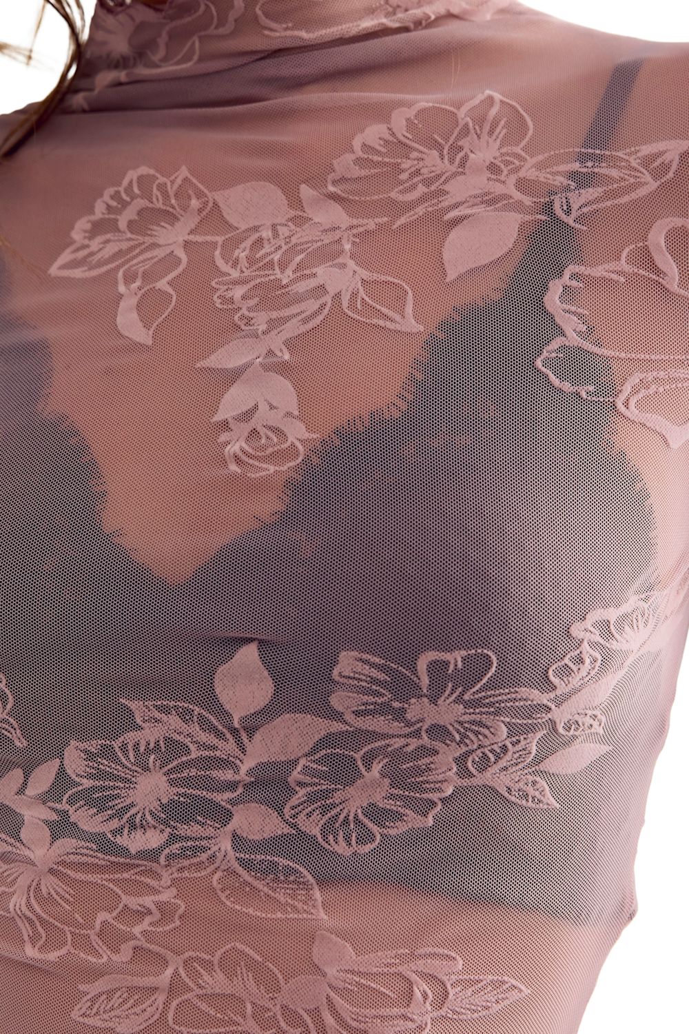 A close-up of sheer floral lace lingerie in a muted mauve-pink tone, layered over a black bra.