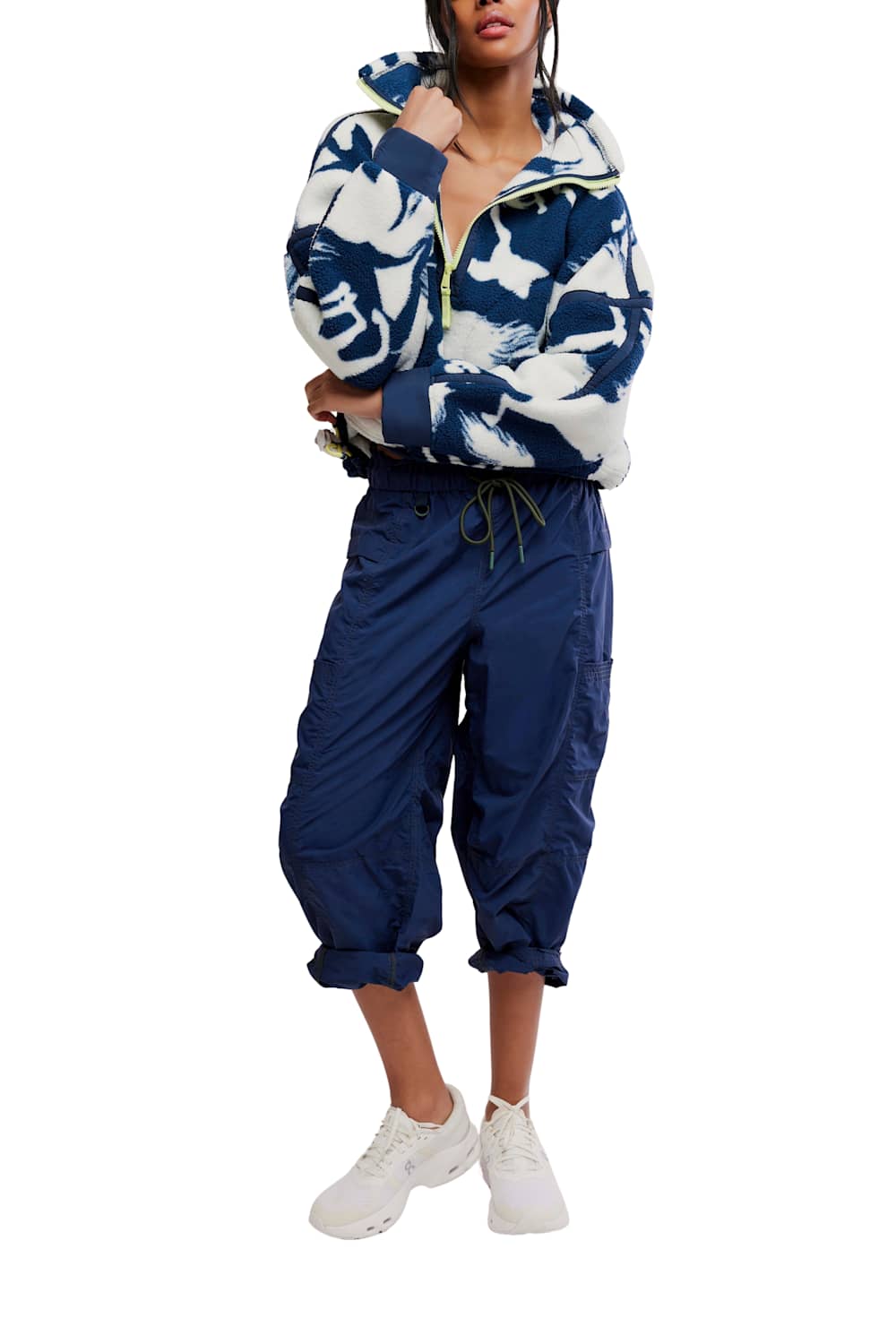 Model wearing the FP Movement Printed Mountain High 1/2 Zip Fleece in navy and white horse print, styled with high-waisted navy cargo track pants pulled up at the calves and white athletic sneakers against a white background.