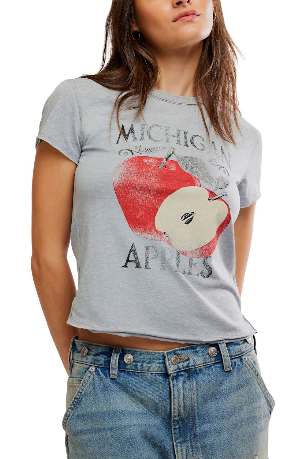 A woman wearing a light gray heathered graphic t-shirt with a distressed red apple print and the words 'MICHIGAN APPLES', paired with blue jeans.
