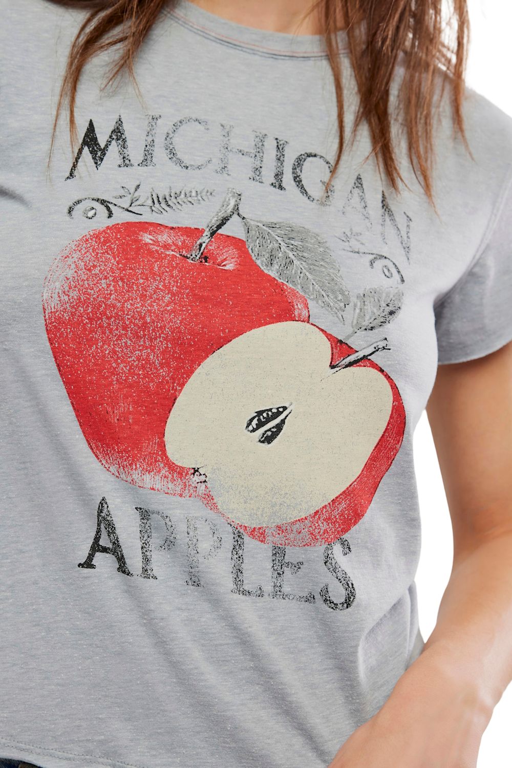 A close-up of a person wearing a heather gray graphic T-shirt featuring a large red apple print with the words 'MICHIGAN APPLES' in distressed black lettering.