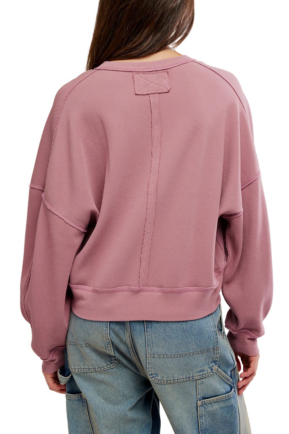 A person shown from the back wearing a dusty rose cropped sweatshirt and blue jeans against a plain white studio background.