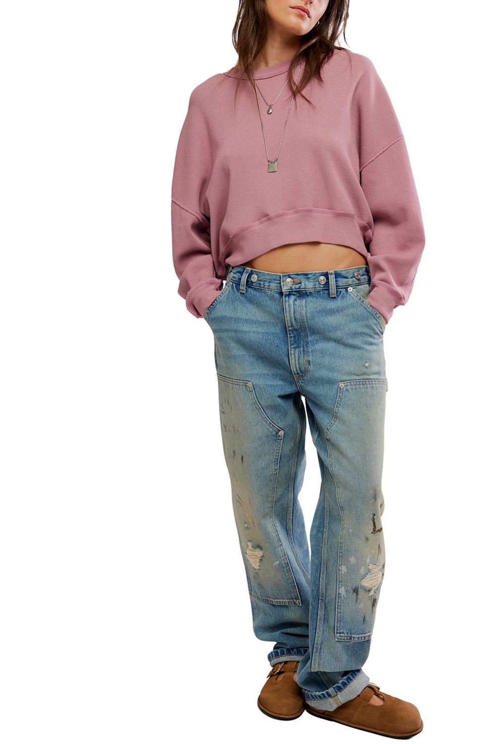 A model wearing a dusty pink cropped sweatshirt, light-wash distressed blue jeans, and brown suede boots, shown from the neck down against a plain white background.
