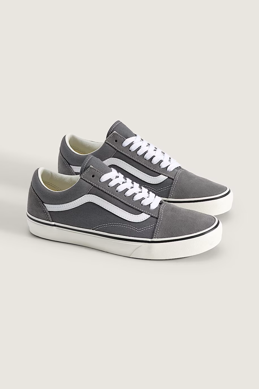 A pair of gray suede Vans Old Skool sneakers with white laces and white side stripes, displayed on a light beige background.
