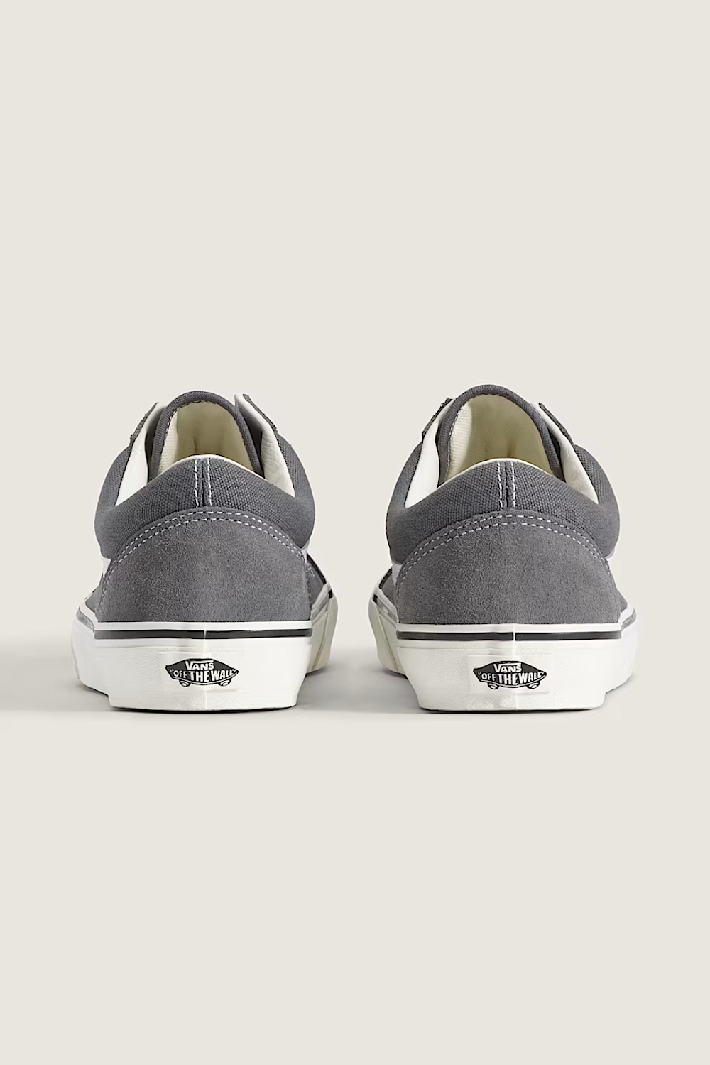 A pair of gray suede Vans Old Skool sneakers with white laces and white side stripes, displayed on a light beige background.