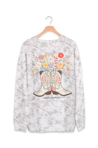 A long-sleeve crewneck sweatshirt featuring a western boot and floral graphic on a light gray and white marbled background, hanging on a wooden hanger against a white background.