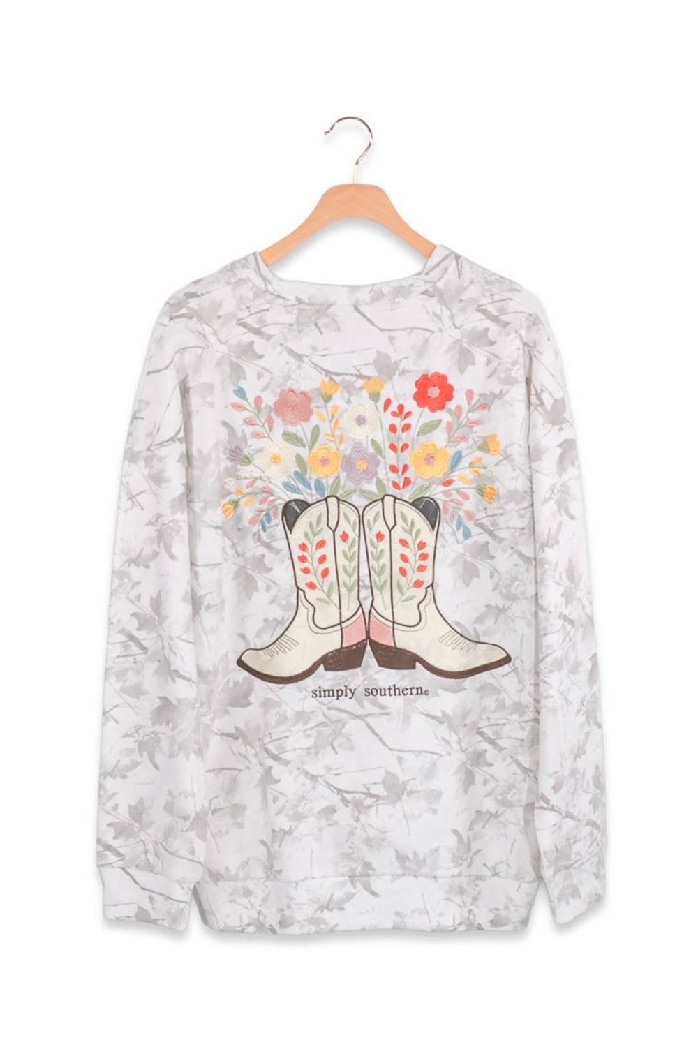 A long-sleeve crewneck sweatshirt featuring a western boot and floral graphic on a light gray and white marbled background, hanging on a wooden hanger against a white background.
