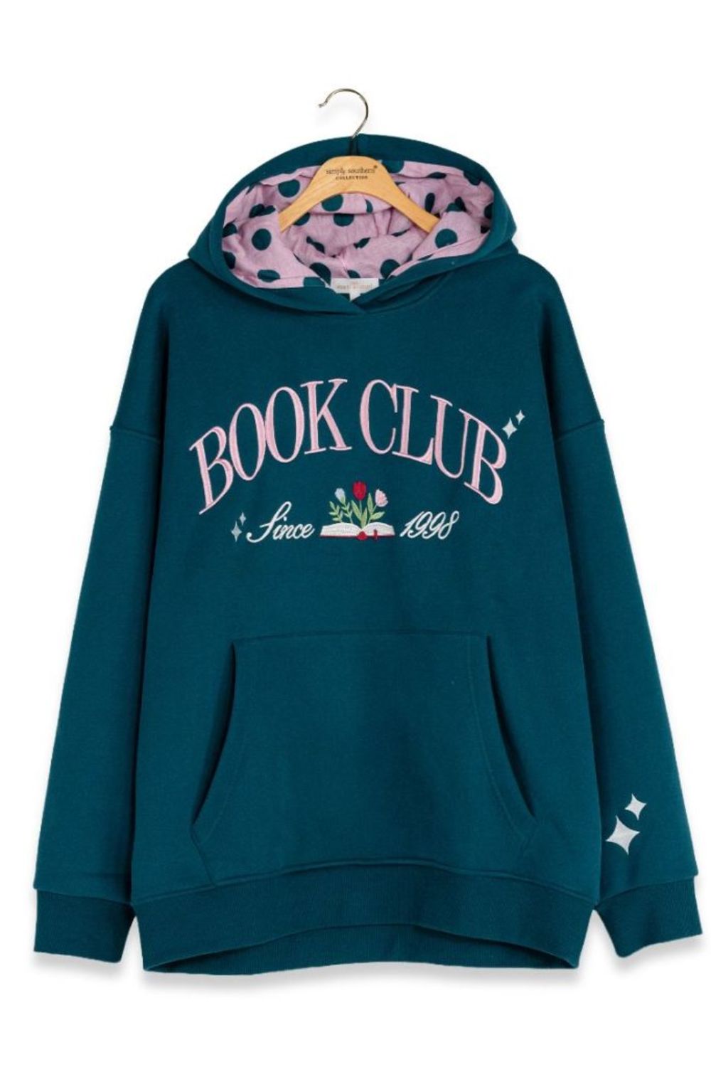 A dark teal blue hoodie with a pink polka-dot lined hood, featuring 'BOOK CLUB Since 1883' printed in pink and white on the front. The hoodie is displayed on a wooden hanger against a plain white background.