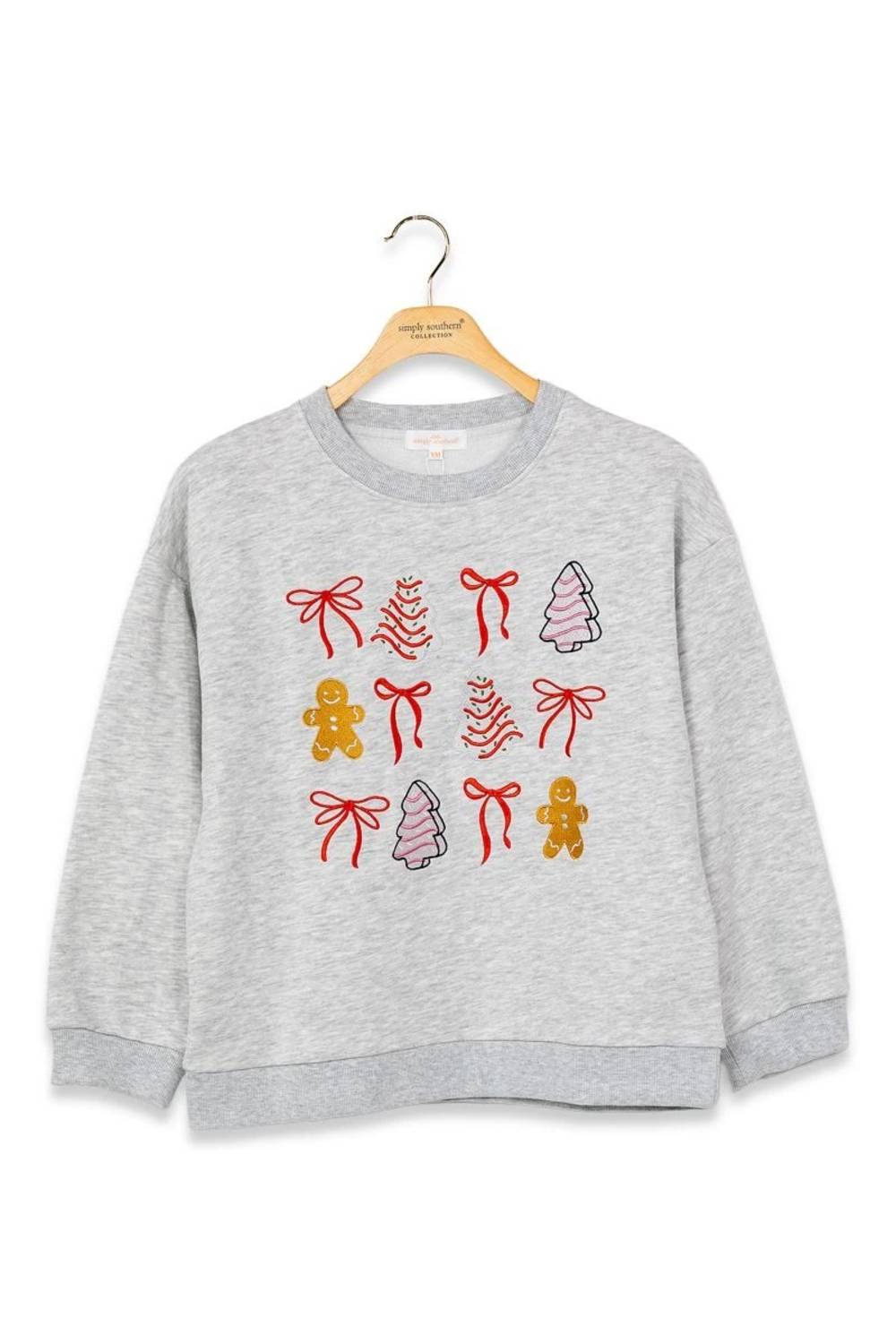 A light gray heather crewneck sweatshirt hanging on a wooden hanger, featuring a festive Christmas pattern of red bows, gingerbread men, and pine trees on the front.