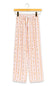 A pair of children's pajama pants hanging from a wooden hanger against a plain white background. The pants are light pink with a vertical pattern of small orange and yellow cartoon figures, and have a white drawstring waist.