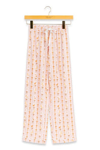 A pair of children's pajama pants hanging from a wooden hanger against a plain white background. The pants are light pink with a vertical pattern of small orange and yellow cartoon figures, and have a white drawstring waist.