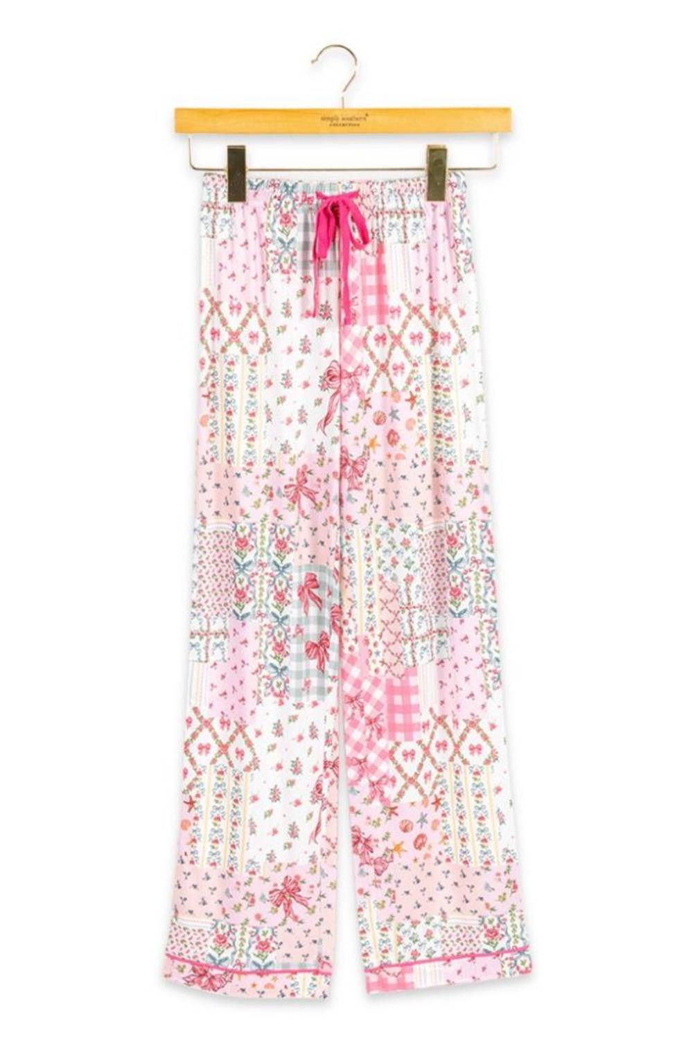 A pair of wide-leg pajama pants with a pink and white patchwork bohemian pattern, hanging on a wooden hanger against a white background.