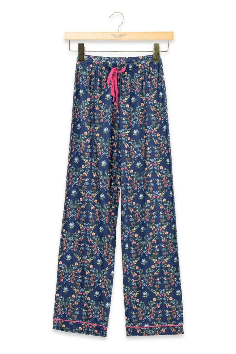 A pair of navy blue pajama pants with a dense multicolor floral print, hanging from a wooden hanger with a pink drawstring waist, against a plain white background.