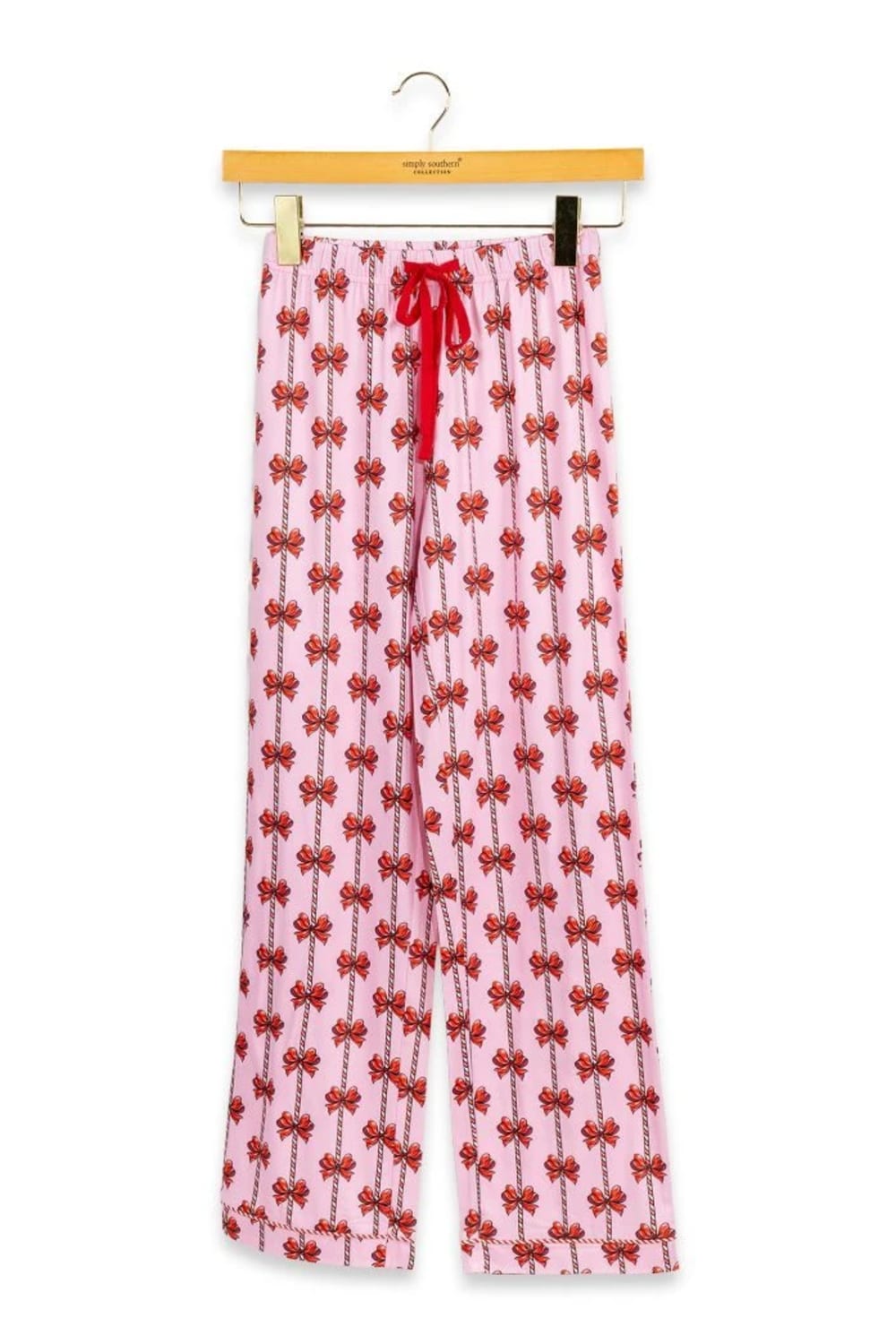 Pink wide-leg pajama pants with a red bow print pattern and a red drawstring waist, hanging on a wooden hanger against a white background.