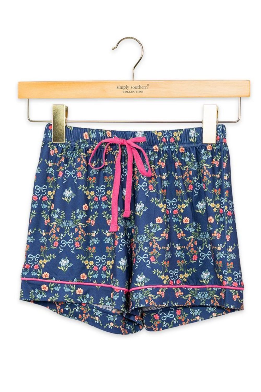A pair of girls' floral print shorts in navy blue with a pink drawstring and pink piping, hanging from a wooden hanger on a white background.