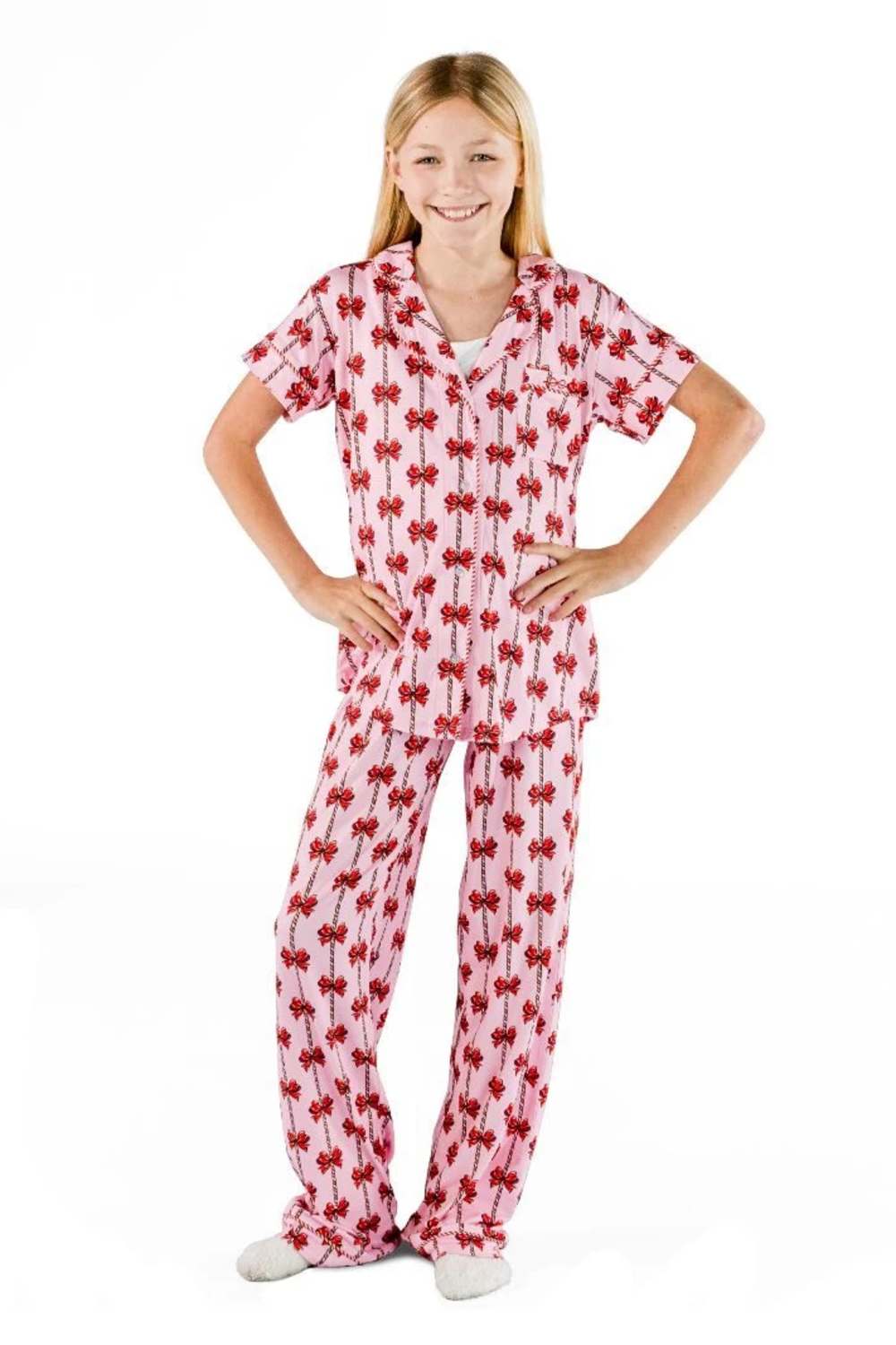 A young girl modeling a two-piece pajama set featuring a pink and red floral pattern, standing against a solid white background.