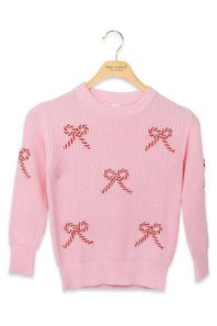 A pink knit sweater with red-and-white candy cane and bow motifs, hanging on a wooden hanger against a plain white background.