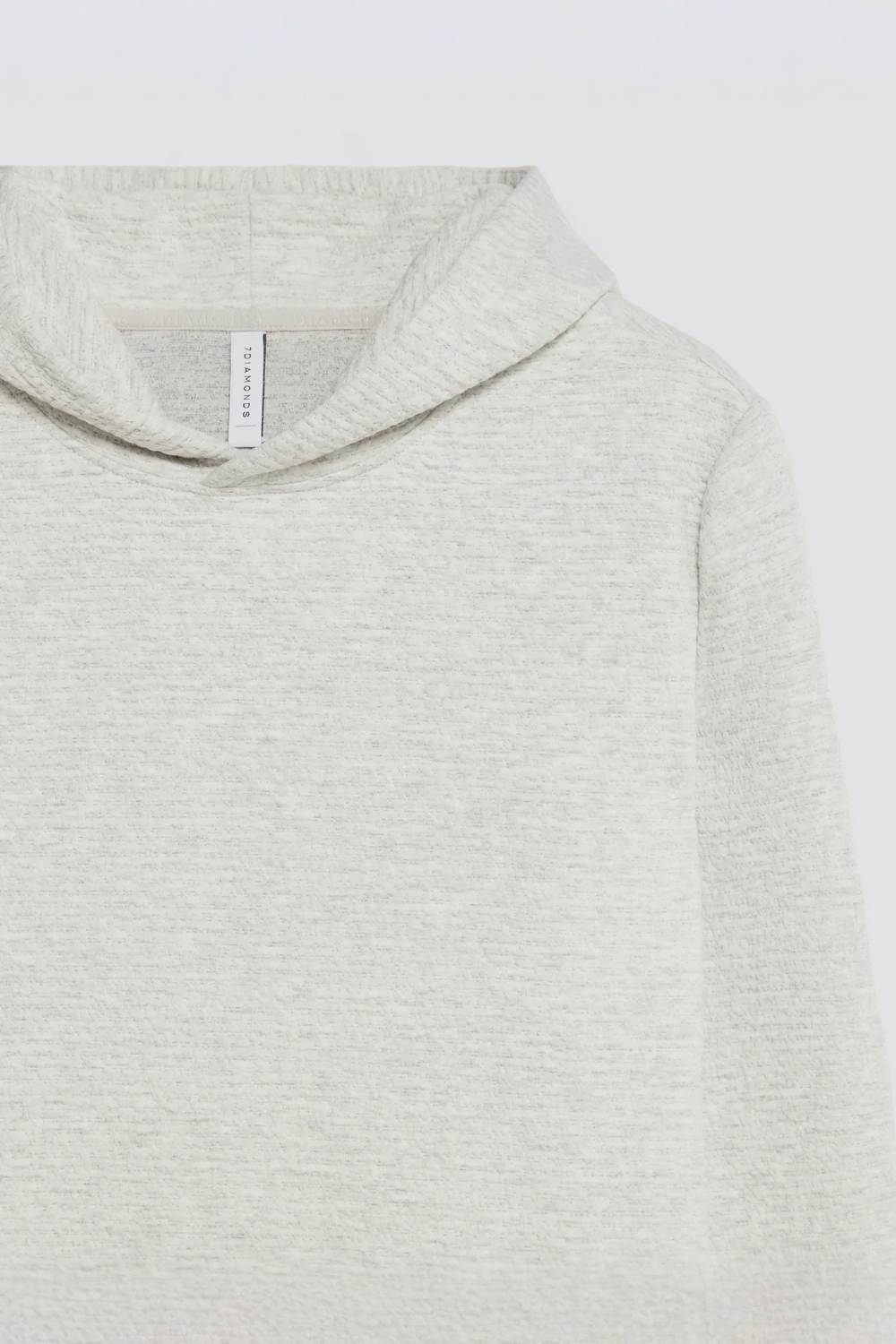 Close-up of a light heather gray hooded sweatshirt, showing the soft knit texture, hood edge, and a small interior neck label.