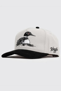 A white structured baseball cap with a black brim, featuring an embroidered loon on the front and the brand name embroidered in black on the side, set against a light gray background.