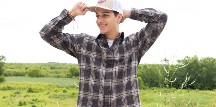 Promotional banner featuring a smiling man wearing a brown and blue plaid button-down shirt and baseball cap while standing in a sunny field.