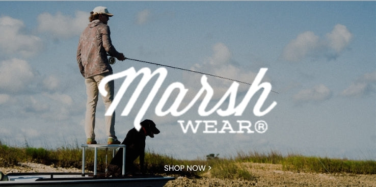 Marsh Wear promotional banner featuring an angler standing on a boat with a fishing rod and a black dog against an open sky and grassy shoreline, with a Shop Now call to action
