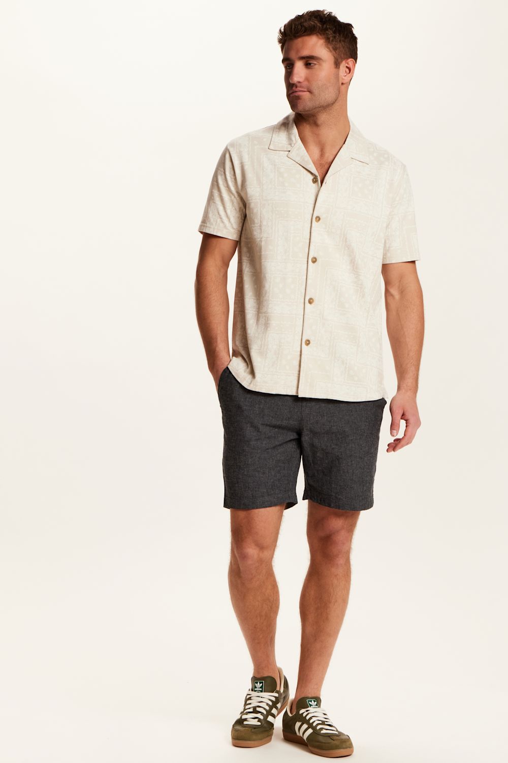 Weatherproof Vintage Bandana Camp Shirt for Men in Tan; Man wearing a beige short-sleeve shirt and dark shorts on a white background