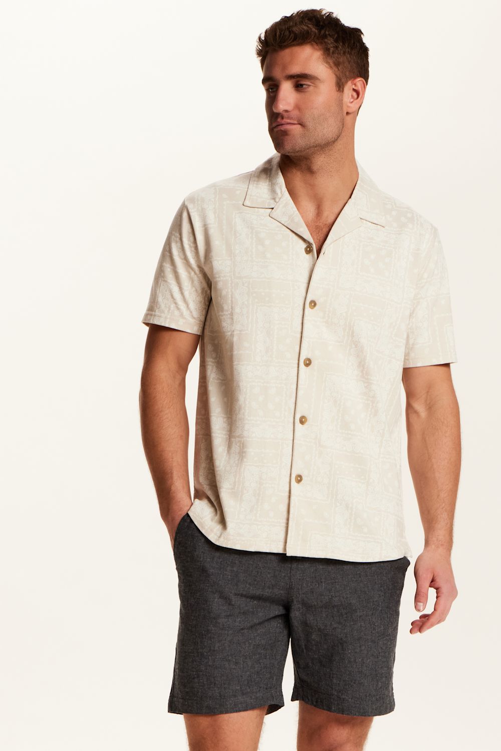 Weatherproof Vintage Bandana Camp Shirt for Men in Tan; Man wearing a beige button-up shirt and gray shorts on a white background