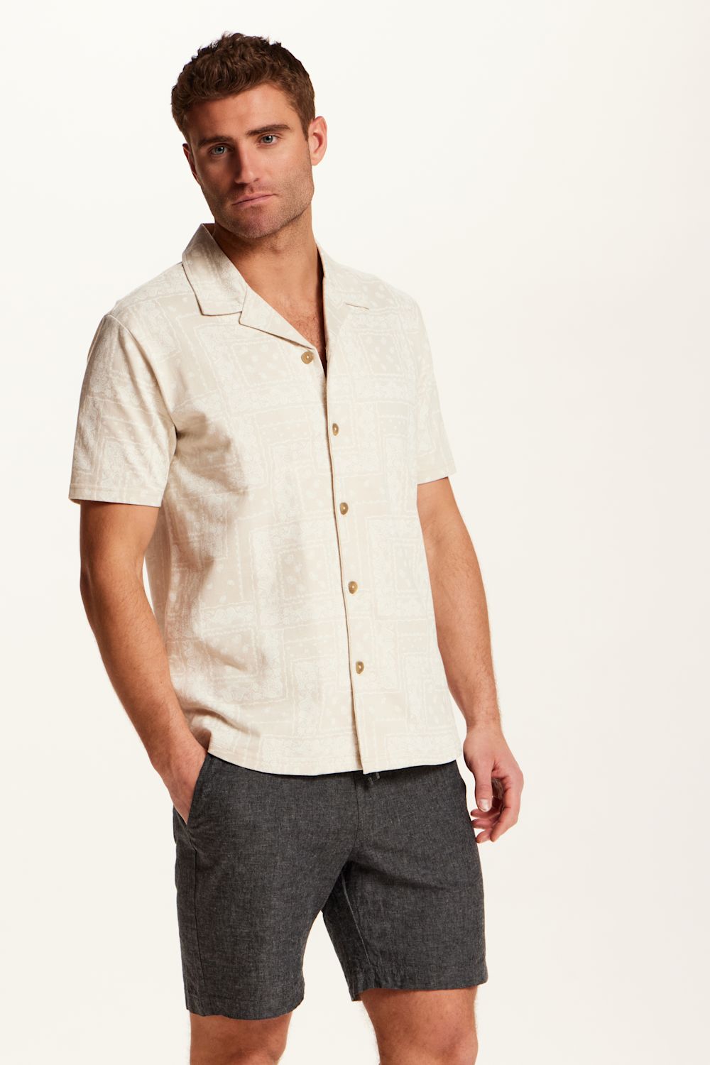 Weatherproof Vintage Bandana Camp Shirt for Men in Tan; Man wearing a beige short-sleeve shirt and gray shorts on a white background