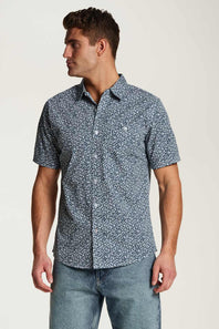 Weatherproof Vintage Poplin Button Up Shirt for Men in Teal; Man wearing a patterned short-sleeve shirt and jeans on a plain background