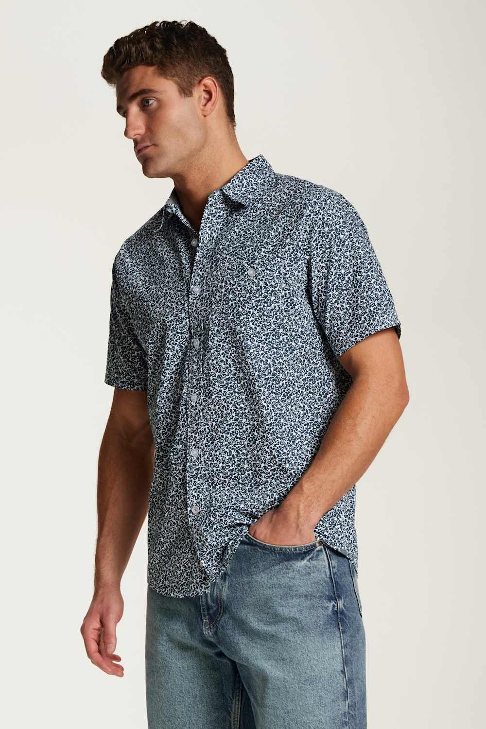 Weatherproof Vintage Poplin Button Up Shirt for Men in Teal; Man wearing a short-sleeve patterned shirt and jeans on a plain background