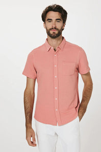 Man wearing a pink short-sleeve shirt and white pants on a white background