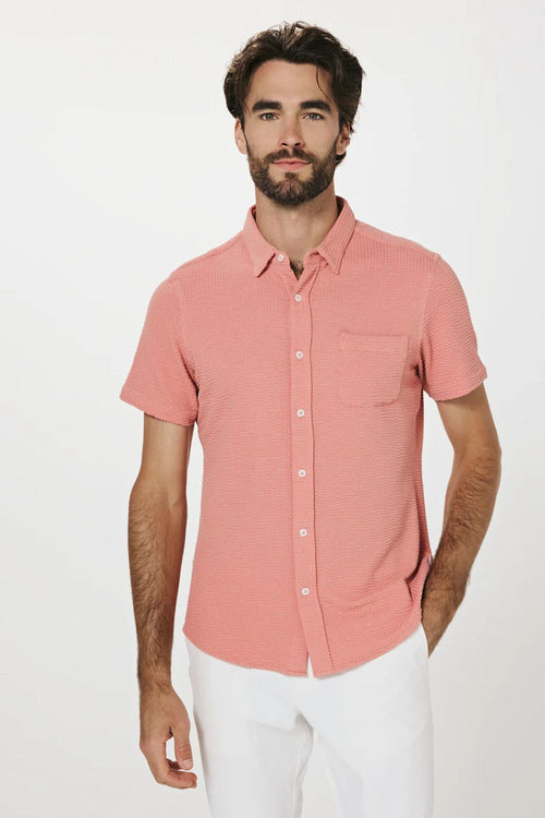 Man wearing a pink short-sleeve shirt and white pants on a white background