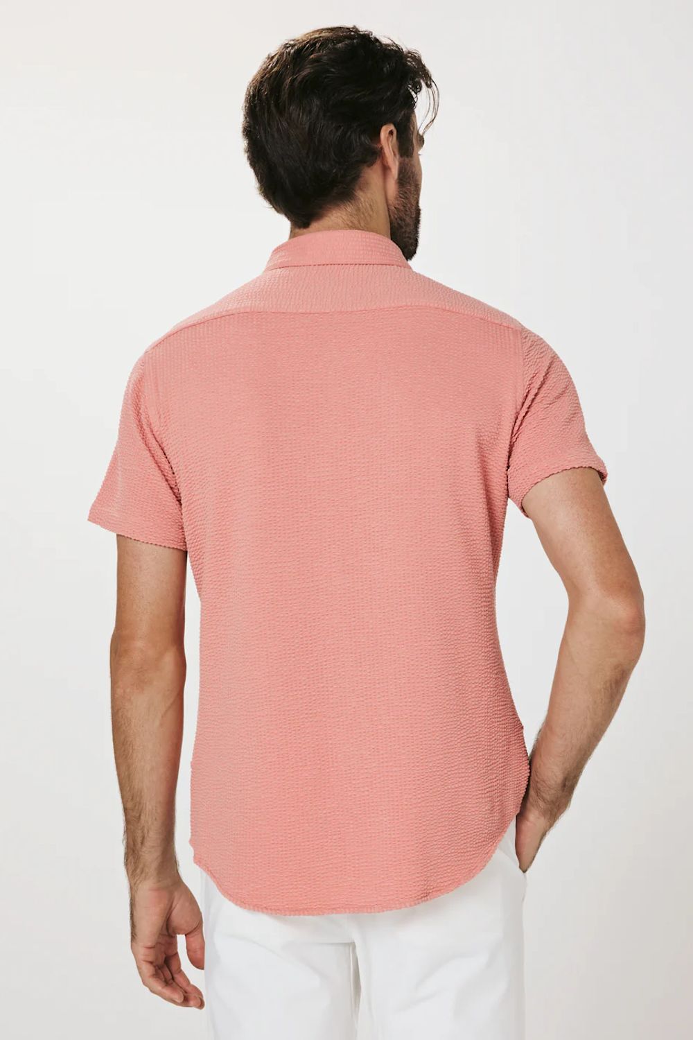Man wearing a pink polo shirt and white pants on a white background