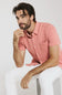 Man wearing a pink shirt and white pants sitting on a white background