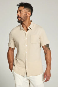 Man wearing a beige short-sleeve shirt against a plain background