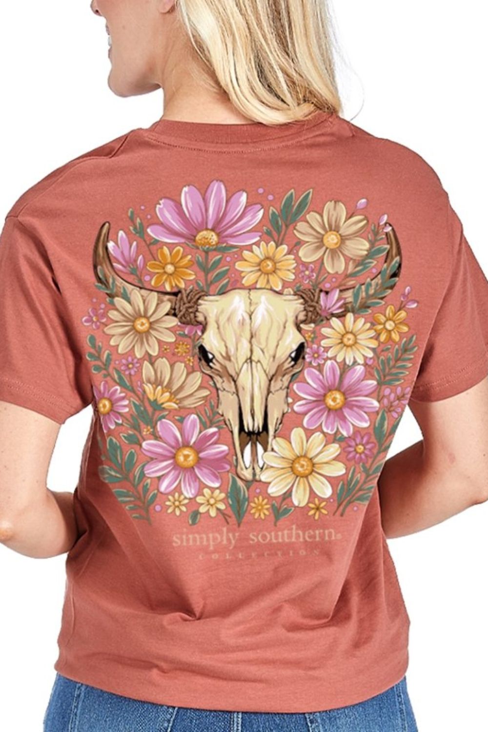 A woman shown from the back wearing a rust-colored short-sleeve t-shirt with a large graphic print of a steer skull surrounded by pink, yellow, and white flowers. The text 'simply southern' is printed below the graphic.
