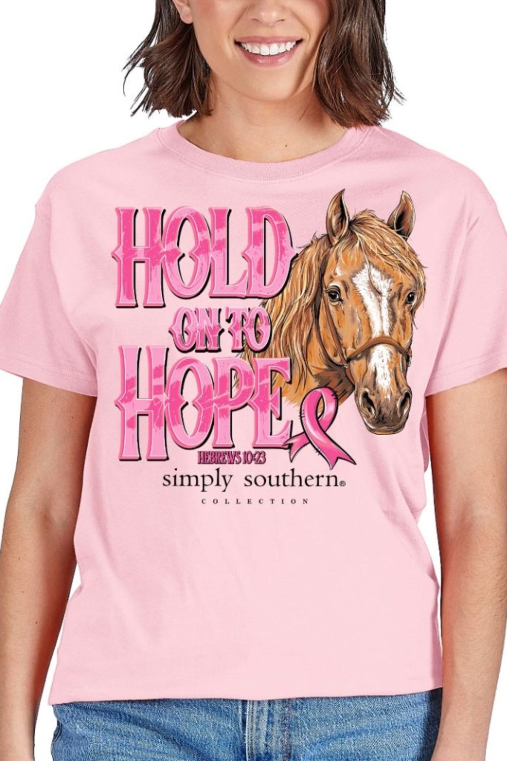 A woman wearing a light pink graphic T-shirt with the words 'HOLD ON TO HOPE' in pink lettering, a brown horse illustration, and 'simply southern' printed below. The photo is cropped from the mouth down to the hips, showing the fit of the shirt.