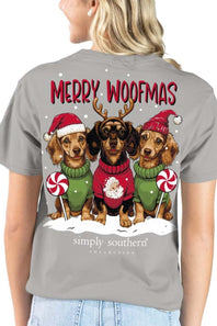A woman wearing a gray short-sleeve t-shirt, viewed from the back. The shirt features a large graphic print of three dachshunds dressed in Christmas sweaters and Santa hats, with the text 'MERRY WOOFMAS' and 'simply southern' collection' printed below.