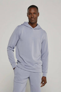 A man wearing a matching light periwinkle blue hoodie and sweatpants set, standing against a neutral light gray studio background.