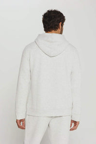 A man viewed from behind wearing a light heather gray hooded sweatshirt and matching sweatpants against a plain light gray studio background.
