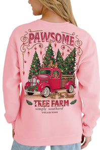 A woman wearing a light pink crewneck sweatshirt, viewed from the back. The sweatshirt features a large graphic print of a red vintage pickup truck carrying Christmas trees, with the words 'PAWSOME' and 'TREE FARM simply southern COLLECTION' printed around it.