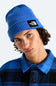 A close-up of a person wearing a bright blue ribbed knit beanie with a black square patch that reads The North Face, paired with a blue and black plaid collared shirt against a light gray background.