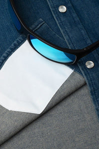 Close-up of a pair of black sunglasses with blue mirrored lenses resting on a folded denim shirt over a gray fabric background.
