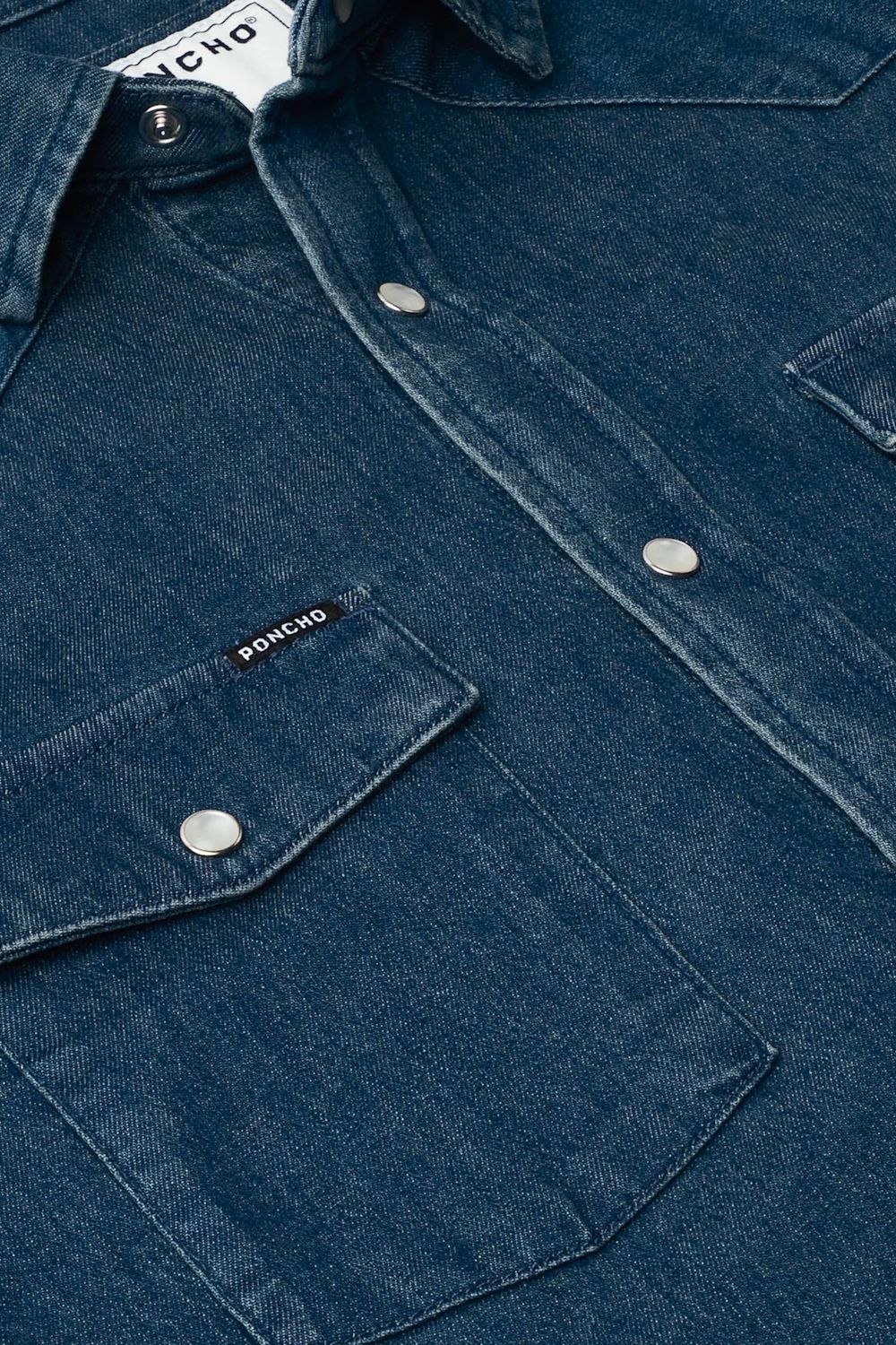 Close-up of a dark blue denim button-up shirt with silver snap buttons and a chest pocket featuring a small visible PONCHO brand tab.