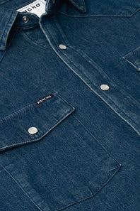 Close-up of a dark blue denim button-up shirt with silver snap buttons and a chest pocket featuring a small visible PONCHO brand tab.