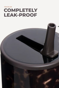 Close-up of a travel tumbler with a dark gray leak-proof lid and straw, featuring a dark brown marbled pattern on the body, with text reading 'TRAVELER COMPLETELY LEAK-PROOF' on a light background.