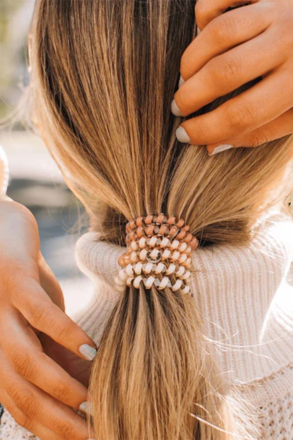 Person styling a ponytail with a decorative hair tie.