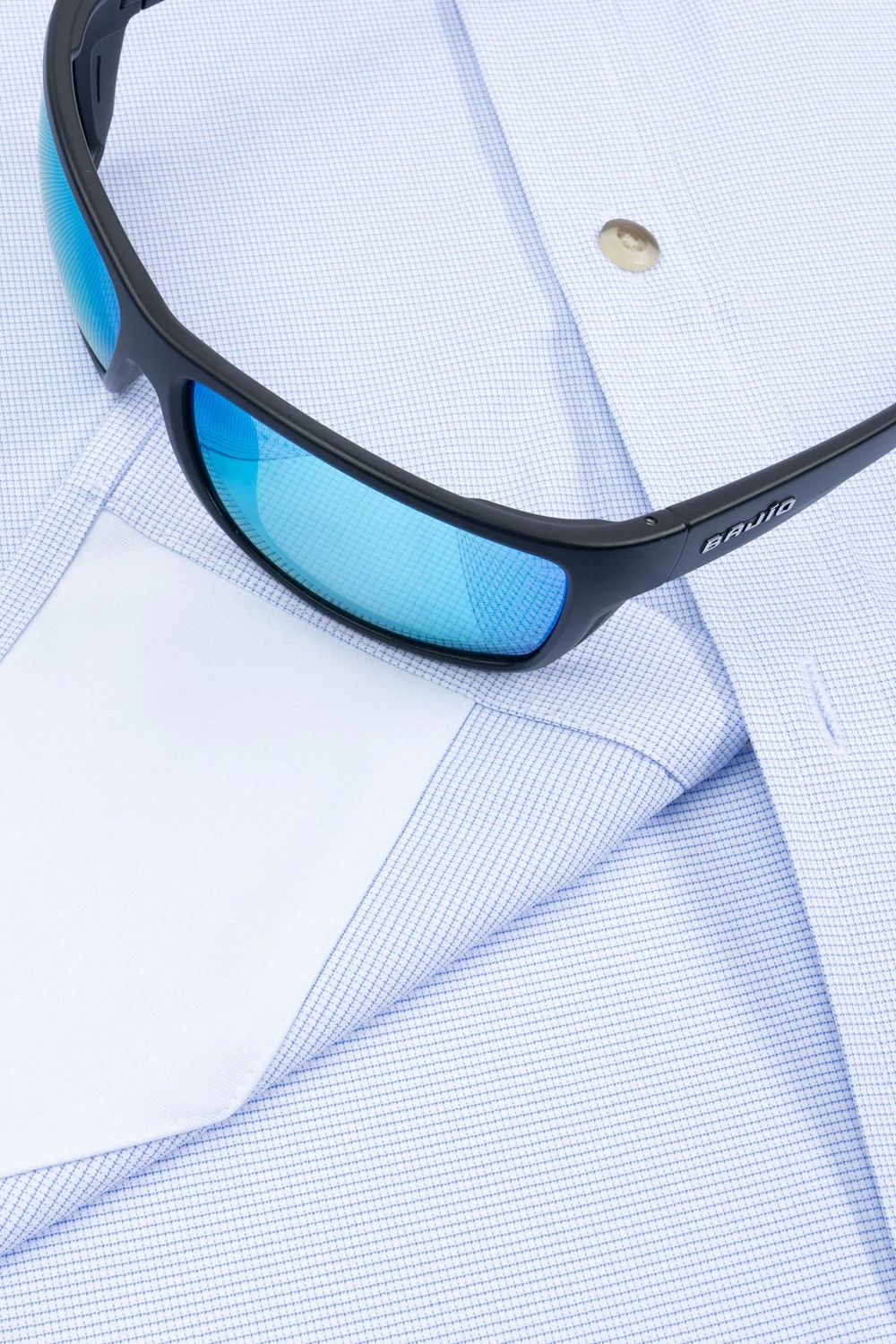 Black sunglasses with blue mirrored lenses resting on a light blue and white micro-check dress shirt.